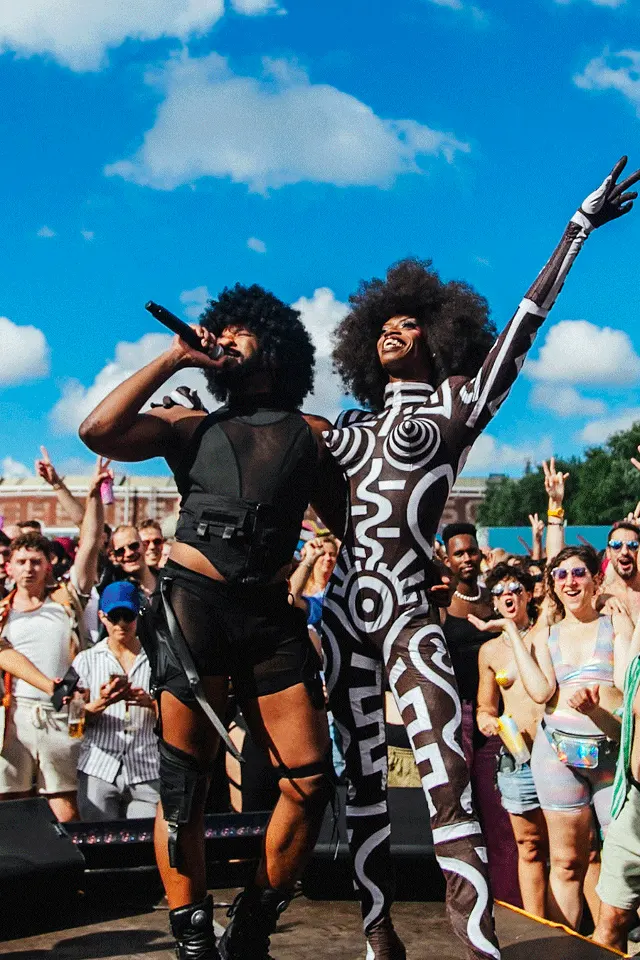 Two performers in black-and-white outfits on stage at Tropikali festival, crowd cheering